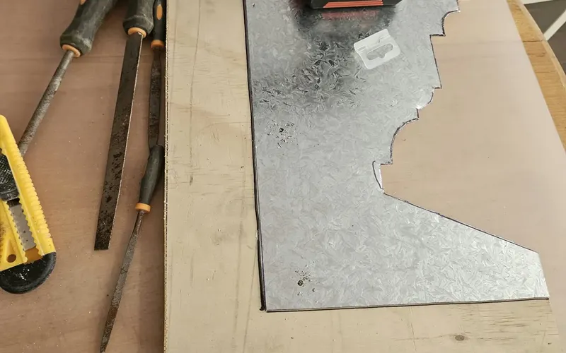 The steel profile template on its plywood backing, with files and a cordless drill on the bench.