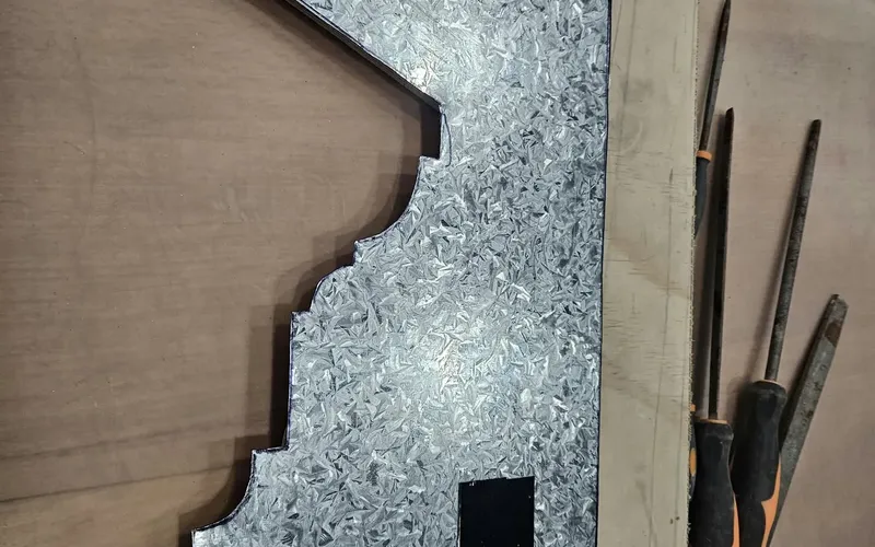 Galvanised steel sheet cut to a stepped and curved moulding profile, mounted on a plywood board, with files beside it.