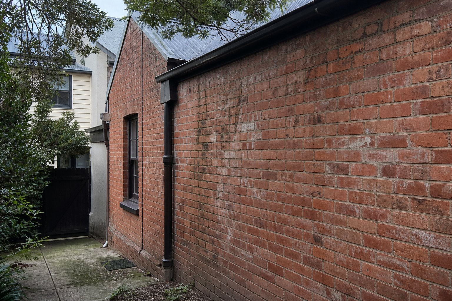 Side elevation of an older Sydney brick house showing weathered brickwork and damp staining