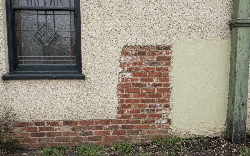Federation cottage roughcast render cut back to brick beside a lime render sample panel, Sydney