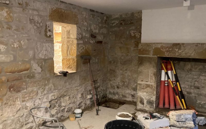 Sydney sandstone basement mid-restoration with repointed stone walls, a window reveal and a sandstone fireplace surround, with site materials on the floor