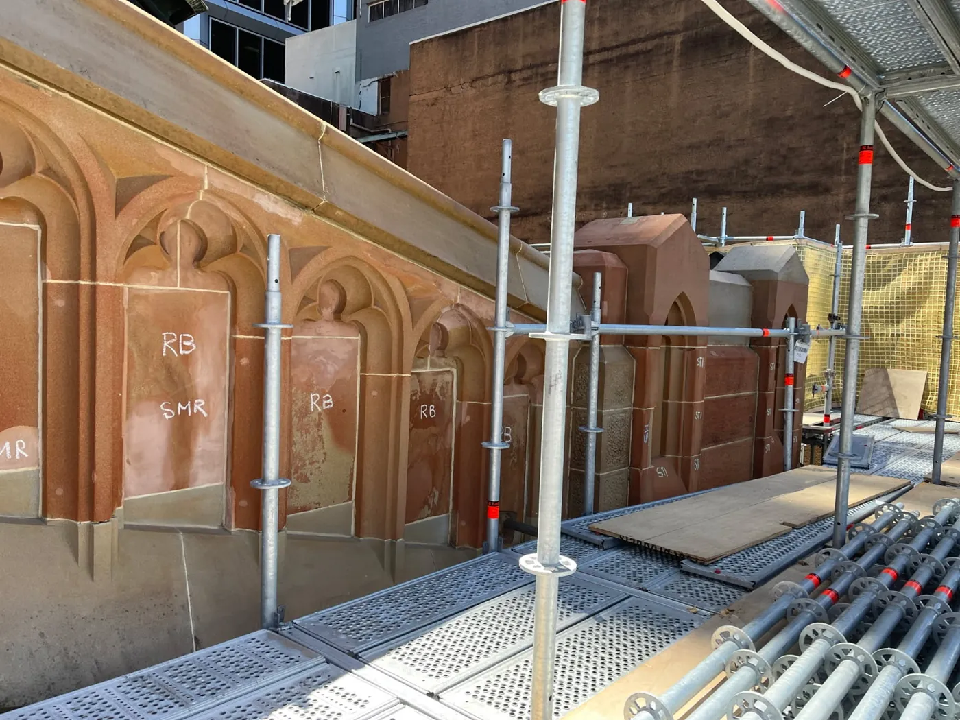 Carved Gothic sandstone arcade under restoration, with conservation markup and scaffolding